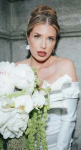 Bride with bold bridal makeup holding a white floral bouquet against a stone wall by Waring Makeup, Ottawa Wedding Makeup Artist.