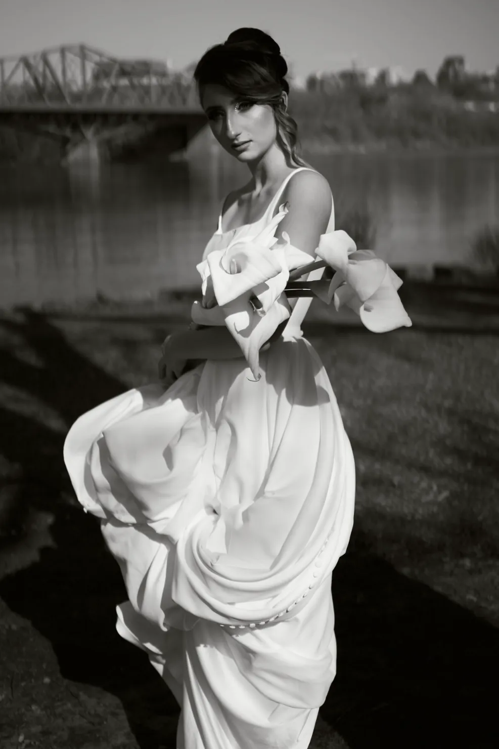 A woman with wedding makeup in a wedding dress holding a bouquet of flowers near a river