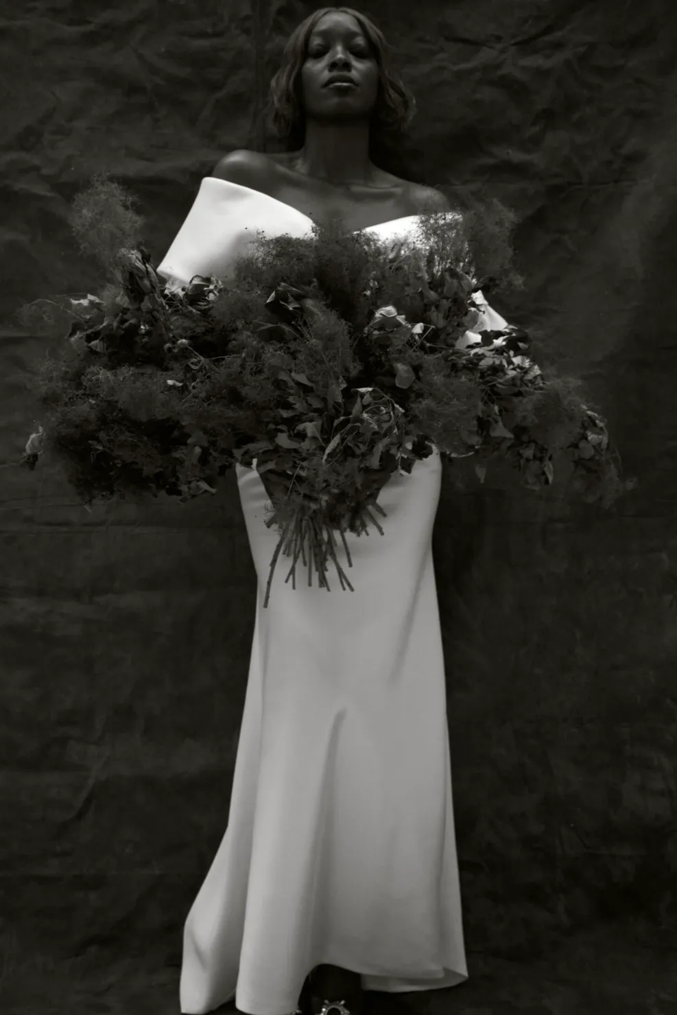 A woman with natural bridal makeup wearing a wedding gown with a huge flower arrangement